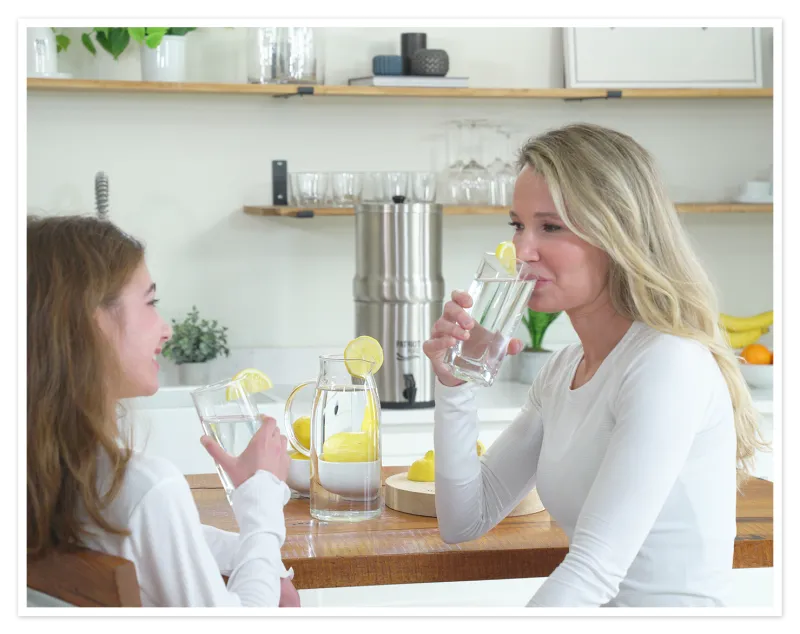 Mother and daughter drinking filtered water together in their kitchen