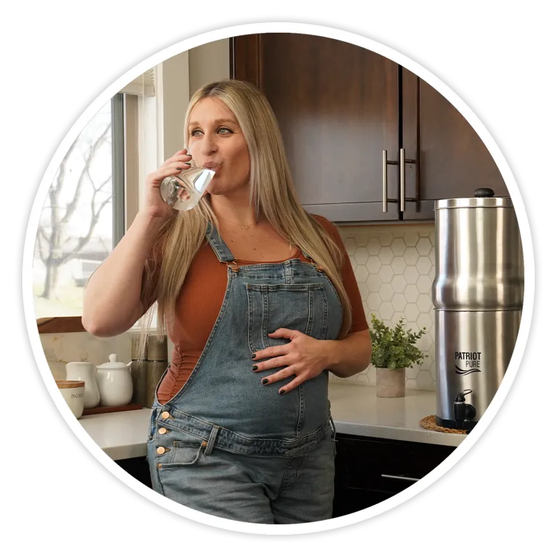 Woman drinking filtered water in her kitchen with Patriot Pure system visible
